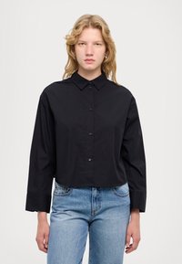 Camicia nera con colletto, maniche lunghe e orlo accorciato. Realizzata in tessuto liscio; presenta bottoni neri e un design complessivo elegante.