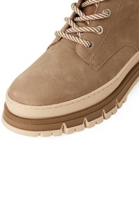 Sneaker in pelle tan con finitura testurizzata, dotato di lacci beige e una suola in gomma spessa e sagomata di colore marrone a contrasto.