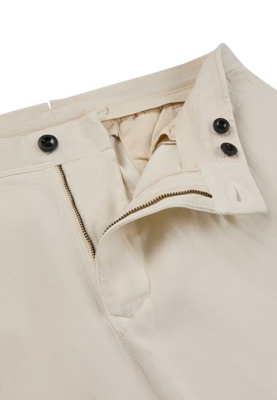 Beige pants with partially open zipper and waistband featuring two black buttons on the inside and one black button on the outside.