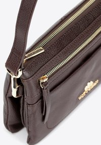 Brązowa skórzana torebka o teksturowanym wykończeniu, z zamkami błyskawicznymi w złotej kolorystyce, odpinanym paskiem i wytłoczonym logo z przodu.