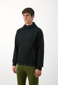 Schwarze Zip-Hoodie mit Logo auf der Vorderseite, verstellbarem Zugband an der Kapuze und seitlichen Taschen. Hergestellt aus weichem Material mit einer lockeren Passform.