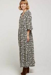 Robe maxi à motif floral noir et blanc avec un décolleté en V, coupe loose et manches trois-quarts, associée à des bottes à talons marron.