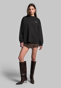 Černá oversize mikina s kulatým výstřihem, která je kombinována s hnědou mini sukní a hnědými koženými botami s vysokým sálem a špičatou špičkou.