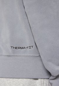 Ljust grå Therma-Fit sweatshirt med mjuk fleece-yta och broderad logotypdetalj nära fållen. Enkelt, rent design.