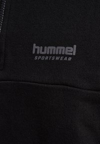 Felpa sportiva nera con zip frontale, texture morbida e logo grigio "hummel SPORTSWEAR" nella zona del petto.