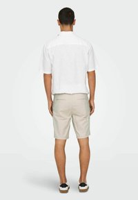 White short-sleeve shirt, beige shorts, and black-accented white shoes. Smooth fabric texture, relaxed fit, and casual design.