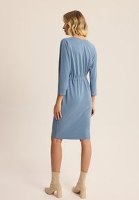 Jasnoniebieska dopasowana sukienka z rękawami 3/4, talią podkreśloną, sięgająca do kolan. Nosić z beżowymi botkami na obcasie.