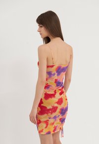 Fargerik, tettsittende kjole med et levende oransje, rødt og lilla tie-dye mønster. Har tynne justerbare stropper og rynkedetaljer bak.