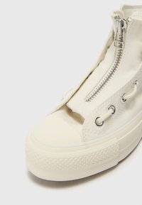 Krämfärgad kanvas högsnörning sneaker med en sidogångjärn, metallöglor och en texturerad gummisula med ett diamantmönster.