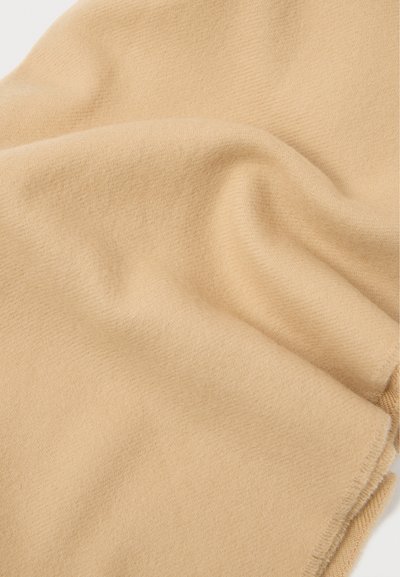 Μαλακό, ανοιχτό μπεζ κασκόλ φτιαγμένο από υφή ύφασμα. Διαθέτει λεία επιφάνεια και φουντωτές άκρες, επιδεικνύοντας ένα ζεστό, ουδέτερο χρώμα.