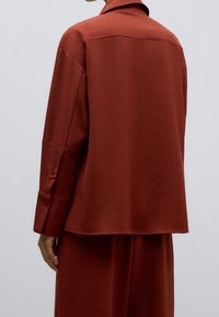 Rostfärgad skjorta i mjukt tyg, med krage, långa ärmar med knäppta manschetter och en lös passform.