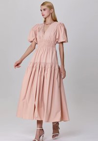 Robe maxi à manches bouffantes en coton doux pêche. Présente un corps smocké et une jupe à niveaux pour une silhouette fluide. Élégant décolleté en V.