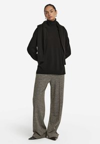 Czarny sweter z kołnierzem, nałożony na pasującą kamizelkę z otwartym przodem, połączony z szerokimi, strukturalnymi spodniami w deseń houndstooth w neutralnych odcieniach.