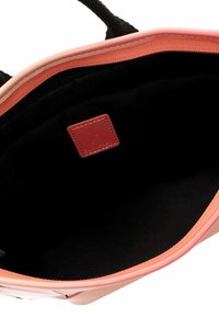 Innenseite einer pinken und schwarzen Handtasche mit glatter Textur, ausgestattet mit einem Logopatch und strukturierter Gestaltung. Abgerundete Kanten und Stoffauskleidung.