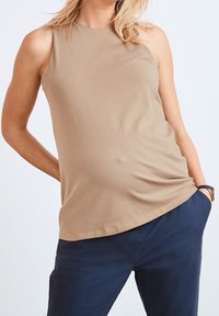 Haut beige sans manches en tissu lisse, avec un col rond et une coupe décontractée, associé à un pantalon bleu marine foncé.
