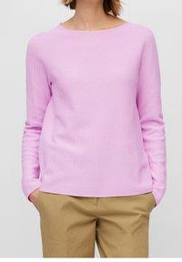 Suéter rosa claro con textura, cuello redondo y mangas largas, combinado con pantalones beige. Diseño sencillo sin adornos adicionales.