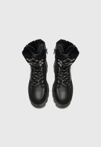 Bottines d'hiver noires avec doublure en fausse fourrure, dotées d'œillets et de lacets métalliques, sur un fond blanc uni.
