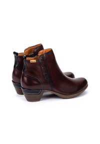 Par de botas de cuero marrón oscuro hasta el tobillo con tacones bajos apilados, cremalleras laterales y costuras decorativas negras en los lados exteriores.