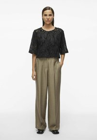 Top negro con textura y mangas cortas, combinado con pantalones de pierna ancha de tiro alto en color marrón claro y calzado negro. Parte delantera plana y textura suave.
