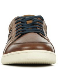 Baskets en cuir marron avec des lacets bleu marine, semelle blanche plate et accents latéraux subtils. Texture lisse avec un design classique de type low-top.