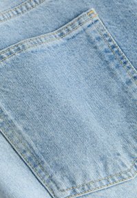 Tissu denim bleu clair avec une poche arrière cousue en fil jaune et une texture de tissage diagonal visible.