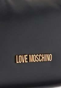 Μαύρη επιφάνεια από δέρμα με υφή, στο κέντρο χρυσό μεταλλικό λογότυπο «LOVE MOSCHINO».