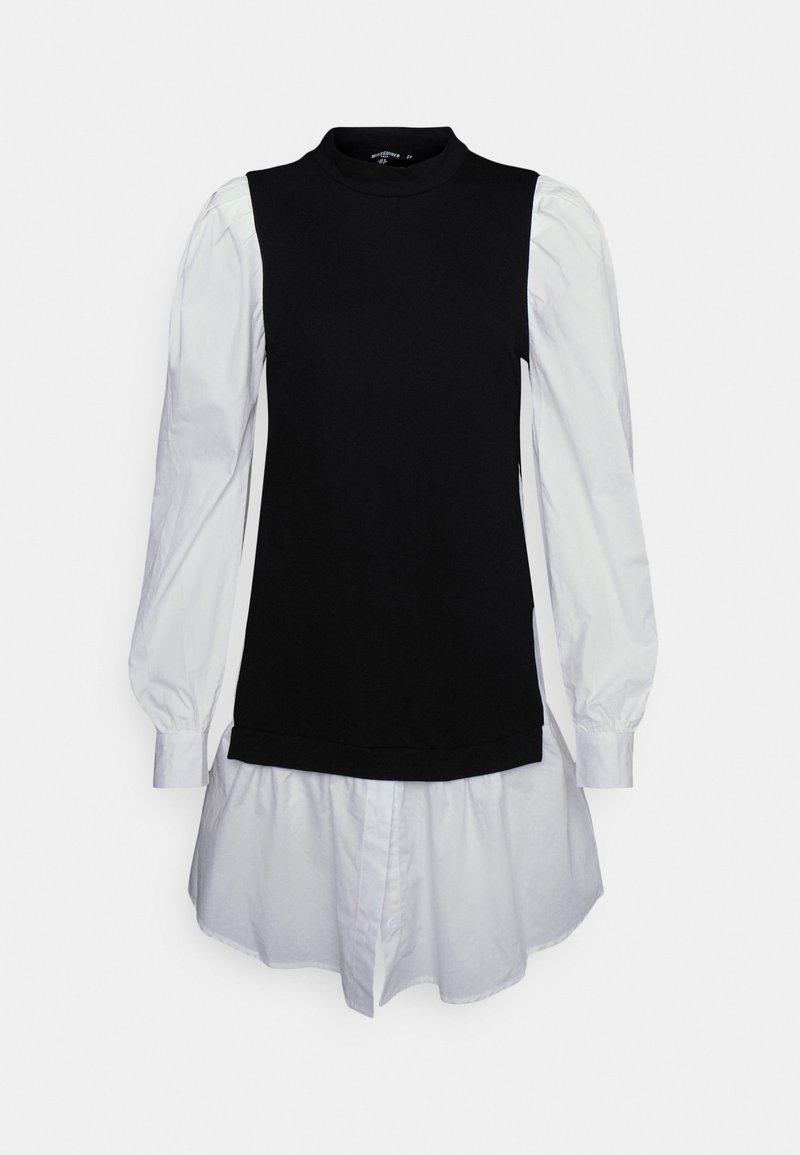 Haut noir ajusté avec un col montant et des manches bouffantes blanches, présentant un ourlet de chemise blanche superposé. Matériaux contrastants et design structuré.
