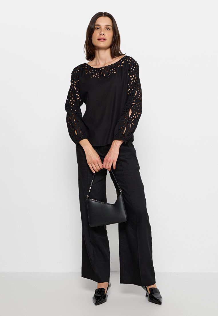 Czarny top z wyciętymi kwiatowymi wzorami na rękawach, zestawiony z czarnymi spodniami w szerokim kroju. Uzupełniony o małą czarną torebkę i buty na szpilkach.