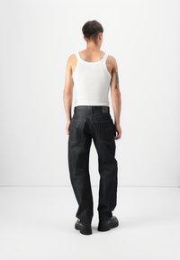 Dark denim jeans with a relaxed fit, featuring two back pockets and a label near the waistband. Worn with a white tank top.
