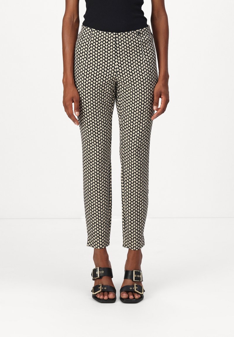 Zwart en crèmekleurige broek met een patroon en een tapered fit, voorzien van een gladde textuur en een elastische tailleband. Gecombineerd met zwarte sandalen.