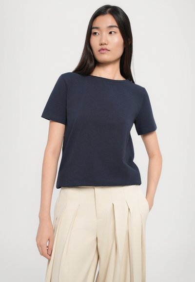 T-shirt blu navy a maniche corte con scollatura rotonda, realizzato in tessuto leggero, abbinato a pantaloni plissettati color crema.