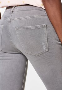 Jean en denim gris avec une vue rapprochée de l'arrière, présentant deux poches et des détails de couture visibles. Texture lisse avec peu d'usure.