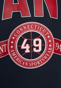 Camiseta azul marino con gráficos en rojo y blanco, que incluyen "CONNECTICUT" y "49" dentro de un emblema circular con temática de baloncesto.