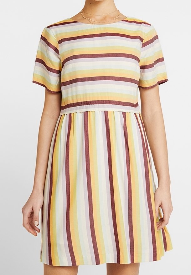 Femme portant une robe courte à manches courtes jusqu'aux genoux avec des rayures horizontales sur le haut et des rayures verticales sur la jupe en jaune, marron et blanc.