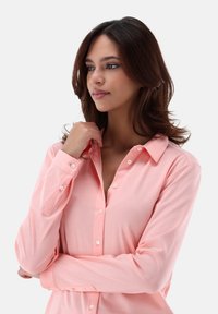 Light pink long-sleeve blouse with button closure, featuring a collar, smooth texture, and a fitted shape for a tailored look.