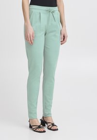 Mintgröna tapered byxor med dragsko i midjan, veck fram och mjukt material, kombinerade med svarta klacksandaler.