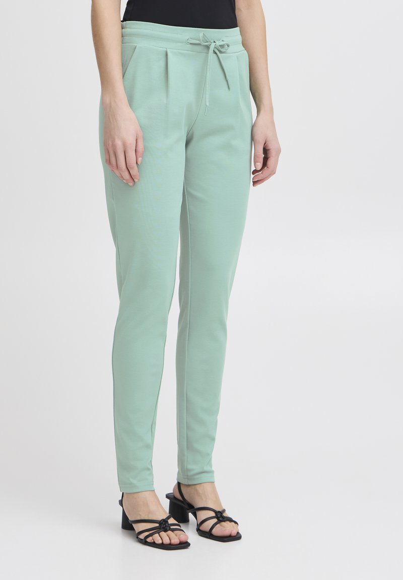 Mintgröna tapered byxor med dragsko i midjan, veck fram och mjukt material, kombinerade med svarta klacksandaler.