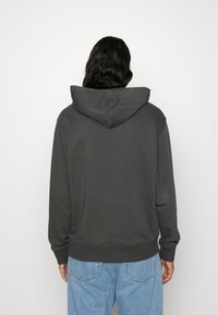 Felpa grigia con cappuccio, dalla texture morbida, maniche lunghe e vestibilità comoda. Presenta un ampio cappuccio e polsini a costine, abbinata a jeans azzurri.