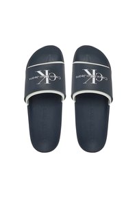 Sandalias de slide azul marino con una tira texturizada que presenta la marca "Calvin Klein Jeans" en blanco. Suela interior suave, diseño plano y estilo minimalista.