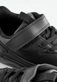 Des baskets noires présentent un dessus en cuir, des accents texturés et une sangle en Velcro pour un maintien sécurisé, avec un design à lacets pour un soutien supplémentaire.