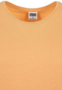 Gros plan sur le col d'un t-shirt orange clair avec une étiquette blanche indiquant la marque Urban Classics, taille XS, fabriqué au Bangladesh.
