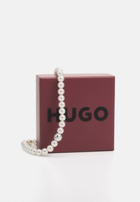 Parelketting met een zilveren accent, tentoongesteld op een kastanjebruine doos met de merknaam "HUGO" in vetgedrukte zwarte letters.