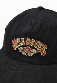 Schwarze Cordhut mit gesticktem "BILLABONG"-Logo in Rot und Gold, mit strukturiertem Oberflächenmaterial und verstärktem Schild.
