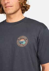 Marineblå bomulls T-skjorte med et sirkulært logo som har et fjell- og solgrafikk i oransje, teal og hvitt, plassert på venstre bryst.