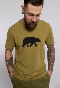 Olijfgroene katoenen t-shirt met een opvallende grafiek van een zwarte beer silhouet op de voorkant. Geweven stof met korte mouwen.