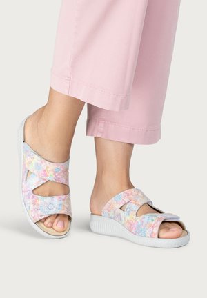 Feet wearing pastel multicolor open-toe sandals with adjustable straps, paired with light pink cropped pants on a neutral background.