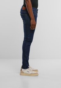 Jeans ajustados de mezclilla azul oscuro con una textura suave, que cuentan con cinco bolsillos y un parche de cuero marrón en la parte trasera de la cintura.