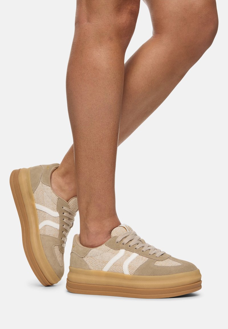 Beżowe sneakersy z białymi akcentami, z chropowatą górą z tkaniny i zamszowymi detalami. Gruba gumowa podeszwa dla dodatkowej wysokości i stabilności.