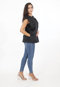 Czarna kamizelka z sztucznego futra bez rękawów, z okrągłym dekoltem i kieszeniami z przodu. Połączona z niebieskimi dżinsami typu skinny i przezroczystymi sandałami na słupku.