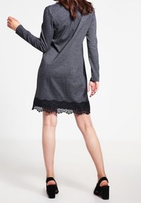 Szara sukienka z długimi rękawami, z czarną koronkową falbanką. Gładka tekstura z dopasowanym krojem i detalem szwu z tyłu. Czarne obcasy.